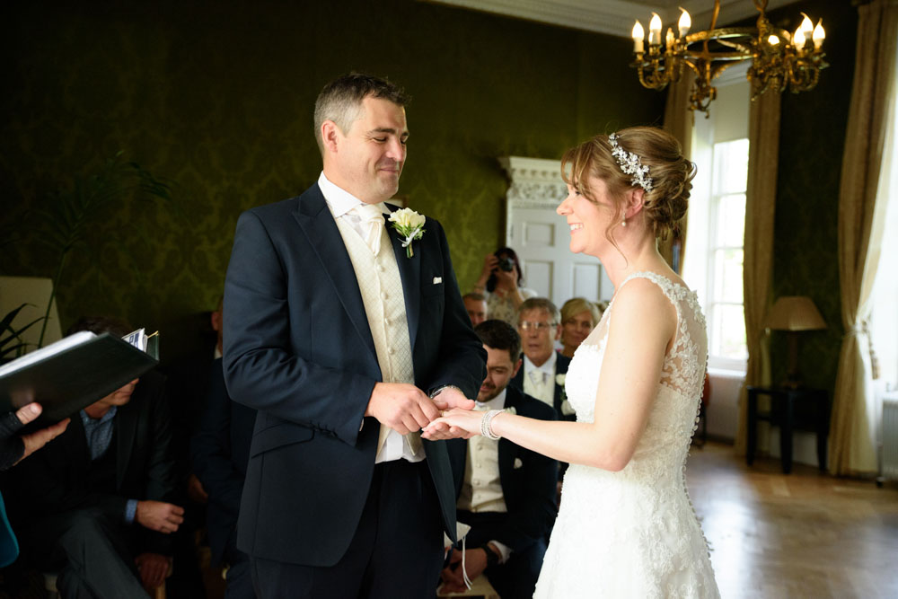 Couple exchange wedding rings with wide smiles during the ceremony.