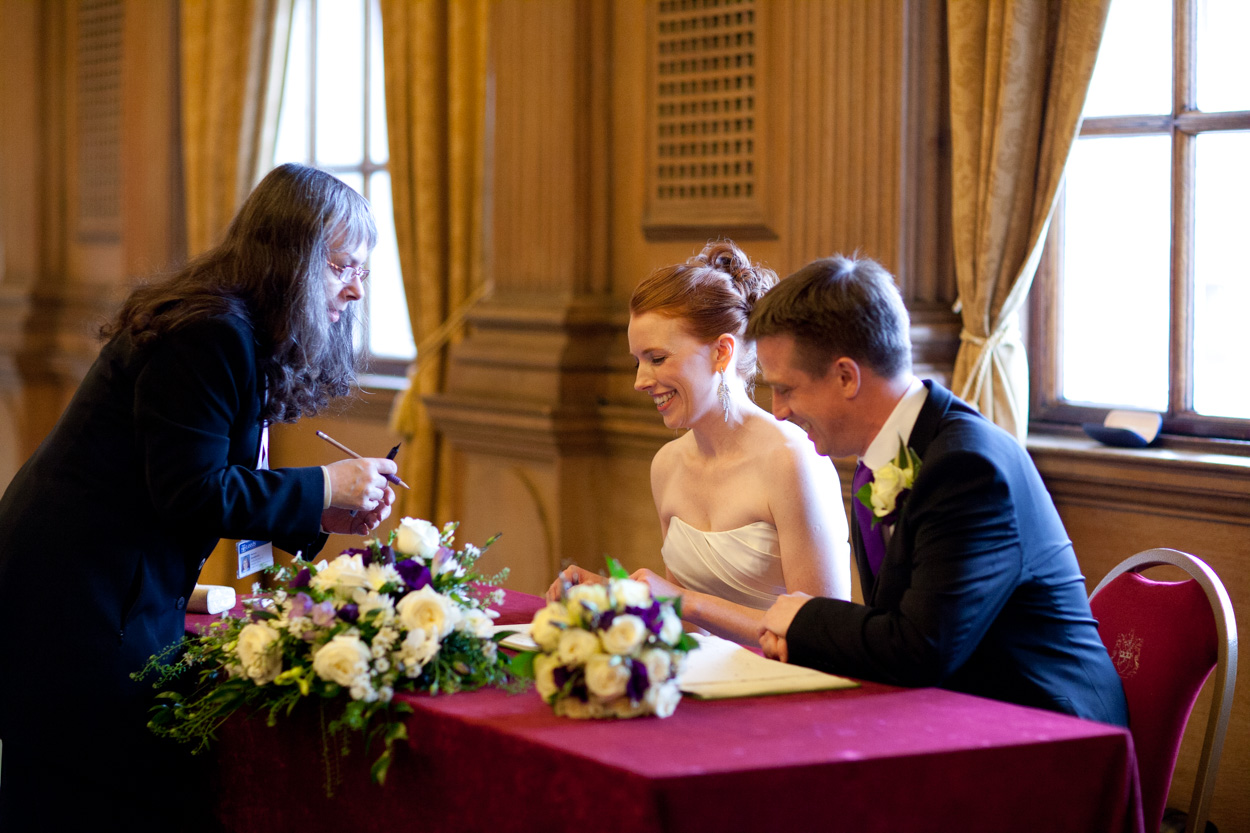 Bride and groom seated together checking the marriage register, smiling as they read.