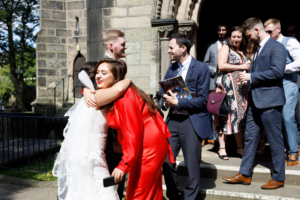 Documentary wedding photo of Kyra hugging friends and family as they exit St Oswald’s Church.
