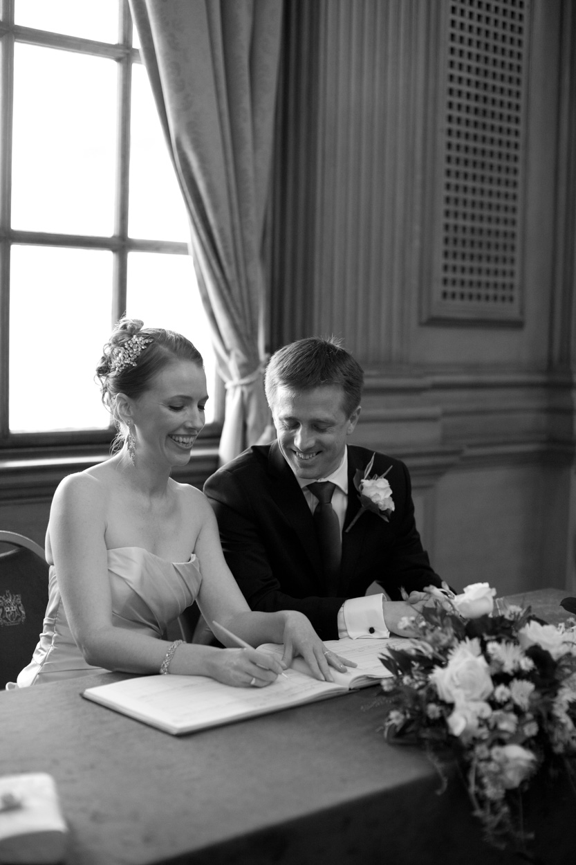 Black and white image of the couple mock-signing the register, laughing together.