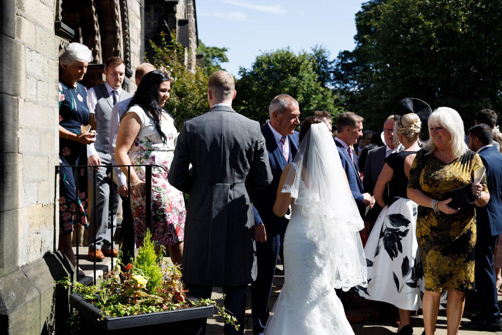 Candid photo of guests mingling outside St Oswald’s Church, with Kyra and Matt in the centre of it all.
