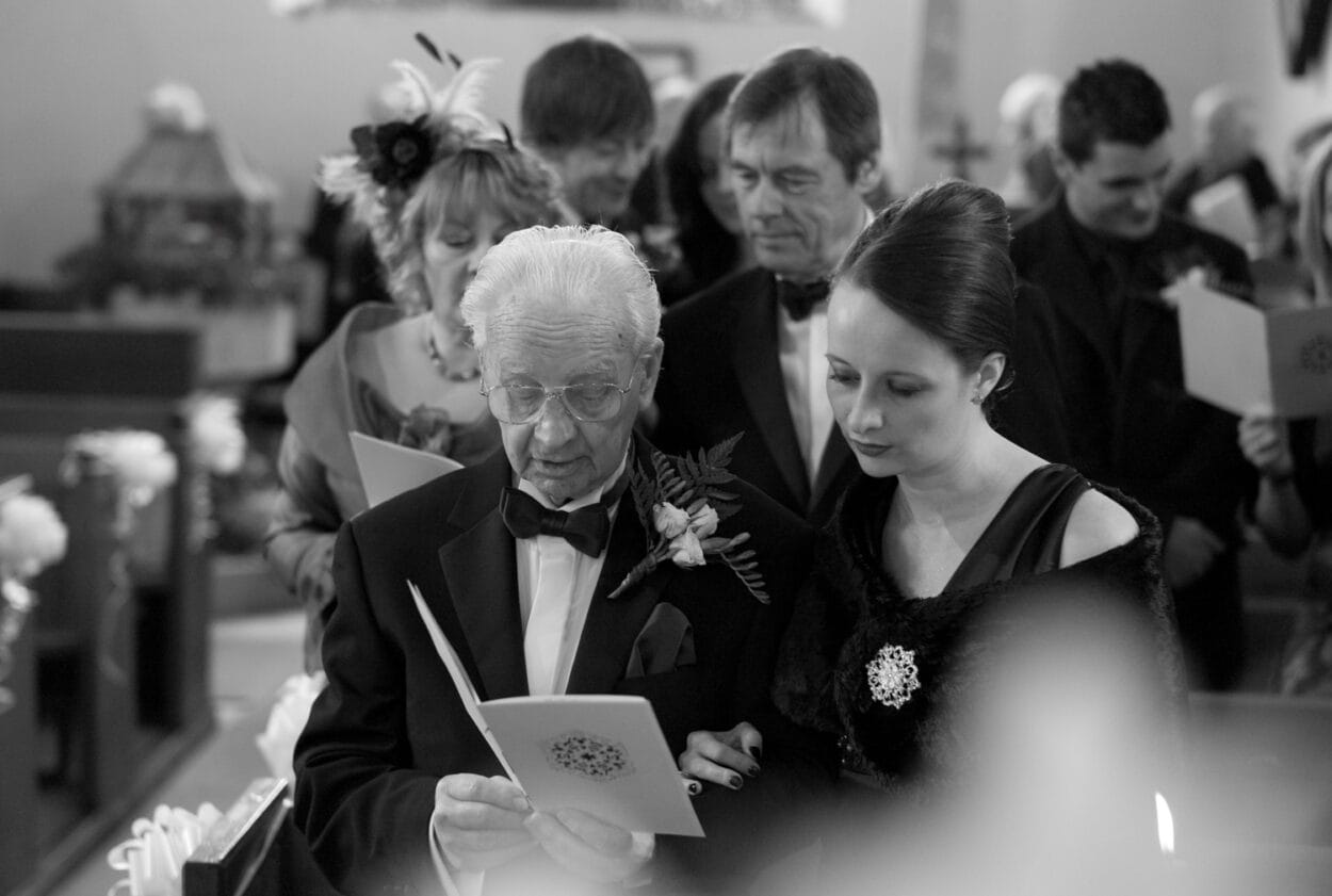 Grandad and granddaughter sing from the order of service in monochrome.