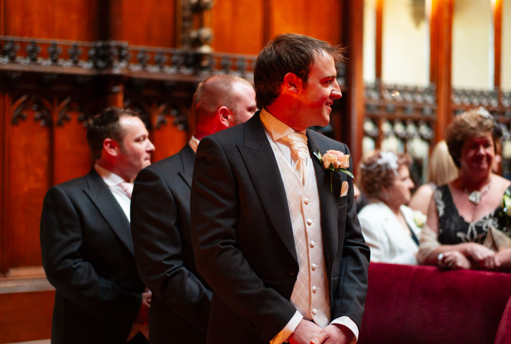 The groom and best men turn and smile as the wedding procession begins.