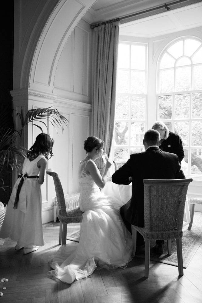 Young bridesmaid leans in as Lisa takes a sip of water, captured in black and white.