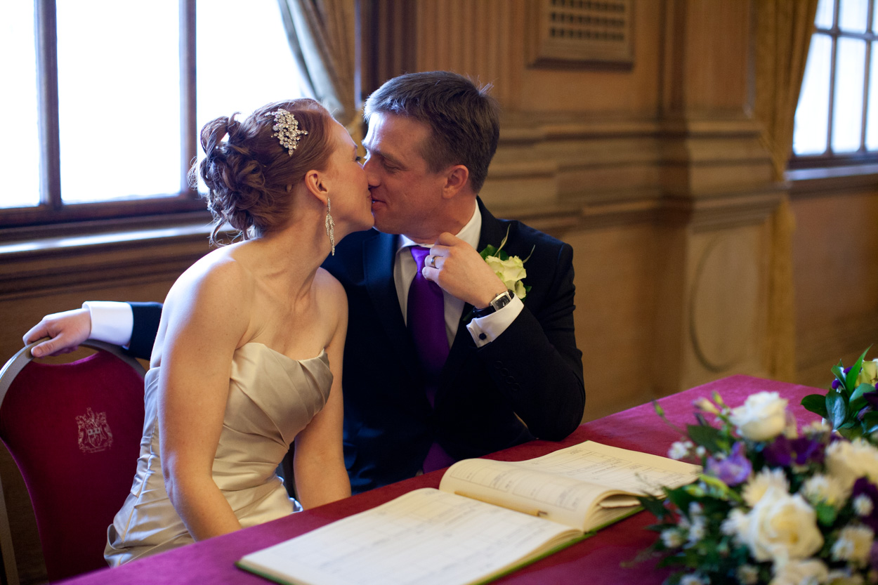 Bride and groom seated, sharing a quiet kiss during the signing.