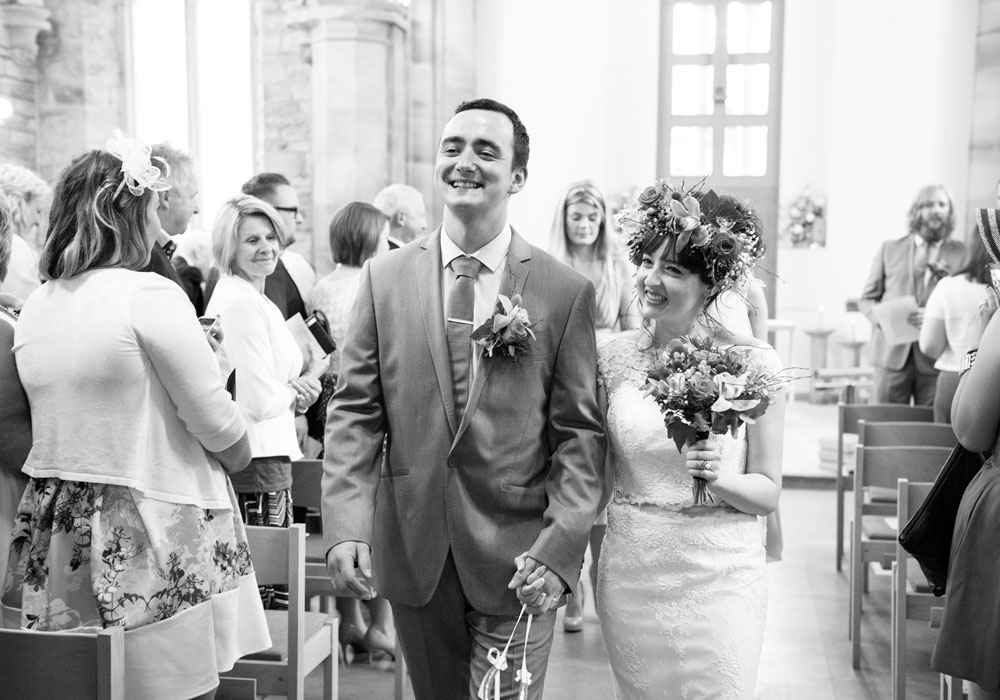 Bride and groom walk hand-in-hand down the aisle, now married.