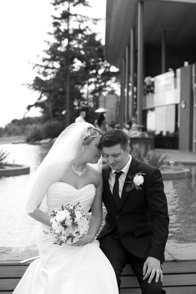 Couple sit by the venue’s waterside in B&W, sharing a natural moment.