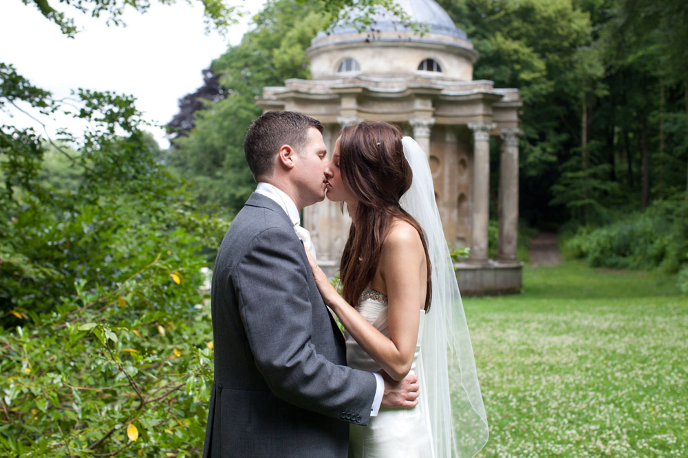 Bride and groom kiss outdoors with the Temple of Apollo in the background at their Leeds wedding
