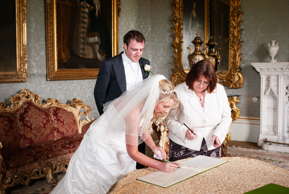 Bride signs the register in soft light, framed by the grandeur of Allerton Castle near Leeds.