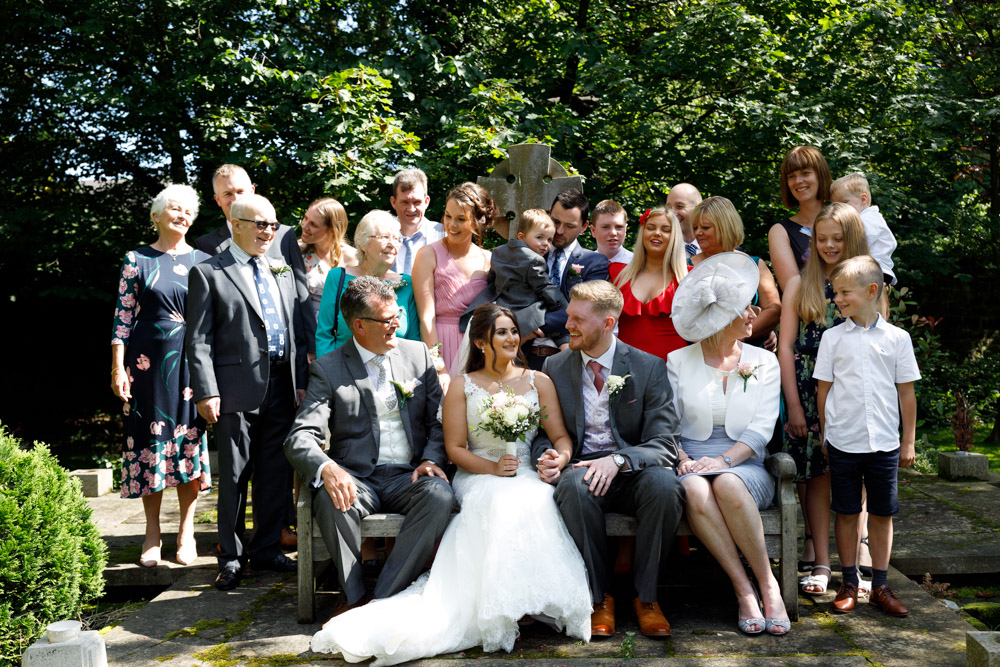 Relaxed family group portrait at St Oswald’s Church, some seated on the bench, others standing and smiling behind.