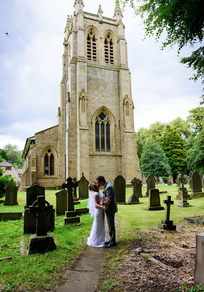 The couple share a kiss on a shaded path beside the church in natural contrast.