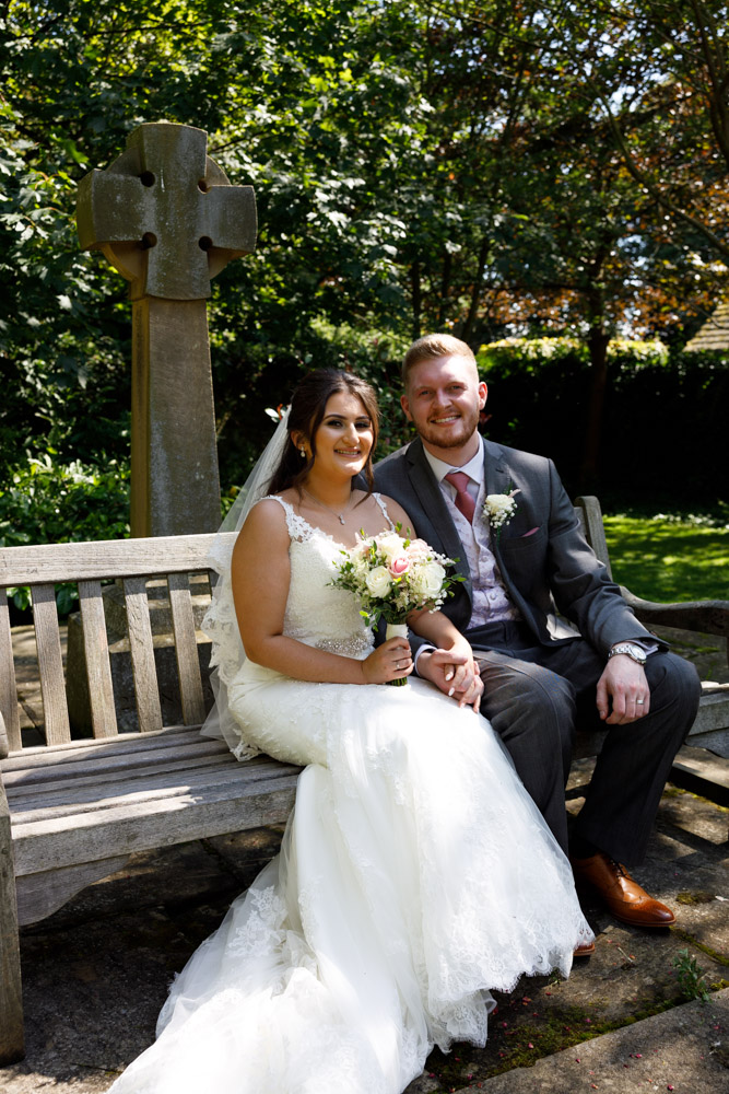 Kyra and Matt sit together at the edge of the church garden, smiling in the gentle sun and shade.