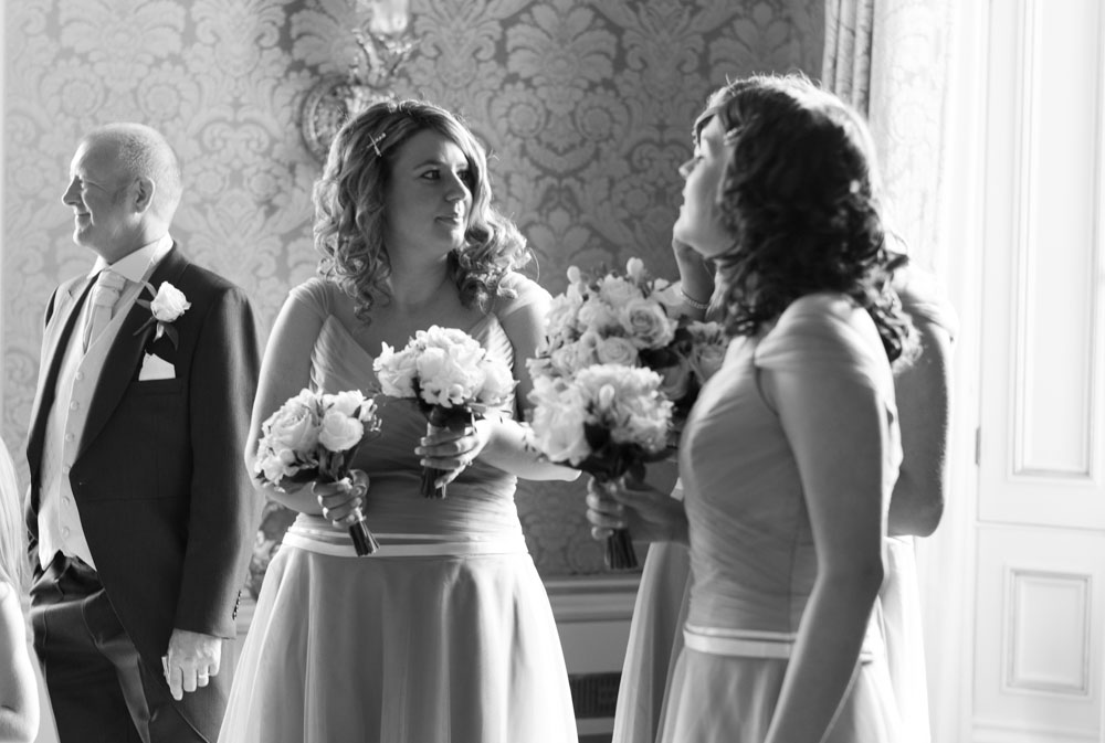 Bridesmaids talking and smiling in black and white, still inside the boardroom at Allerton Castle.