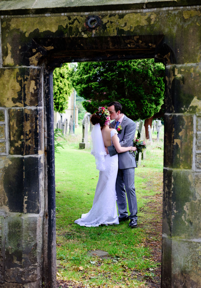 Couple framed through the stone gate at St Paul’s, sharing a colourful kiss.