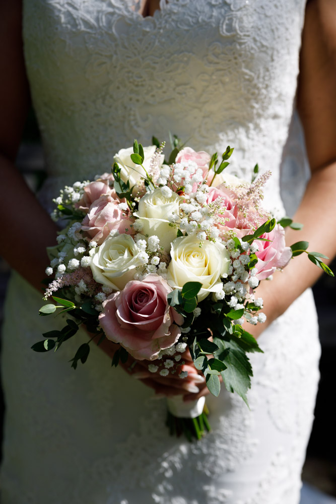 Close-up of Kyra’s pink and white bouquet held against her dress in dramatic summer light.
