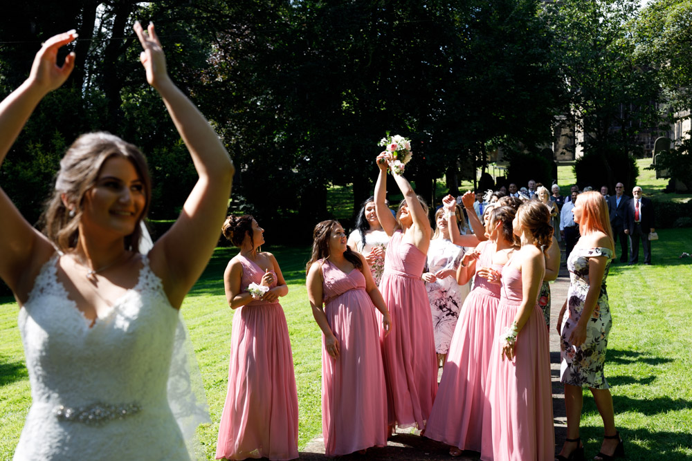Kyra throws her bouquet in the church garden as the bridesmaids and friends eagerly reach for it.