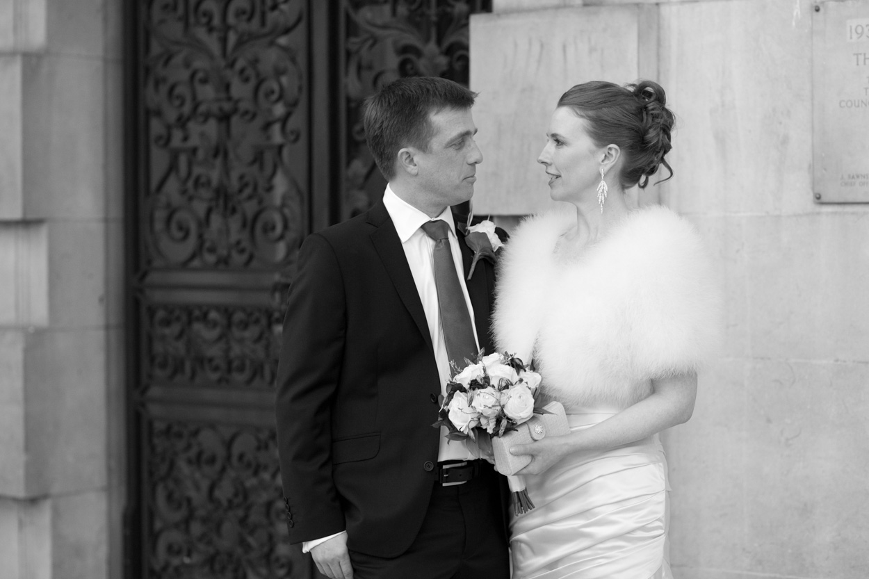 Bride and groom gazing at each other outside the black gates of Leeds Civic Hall in colour.