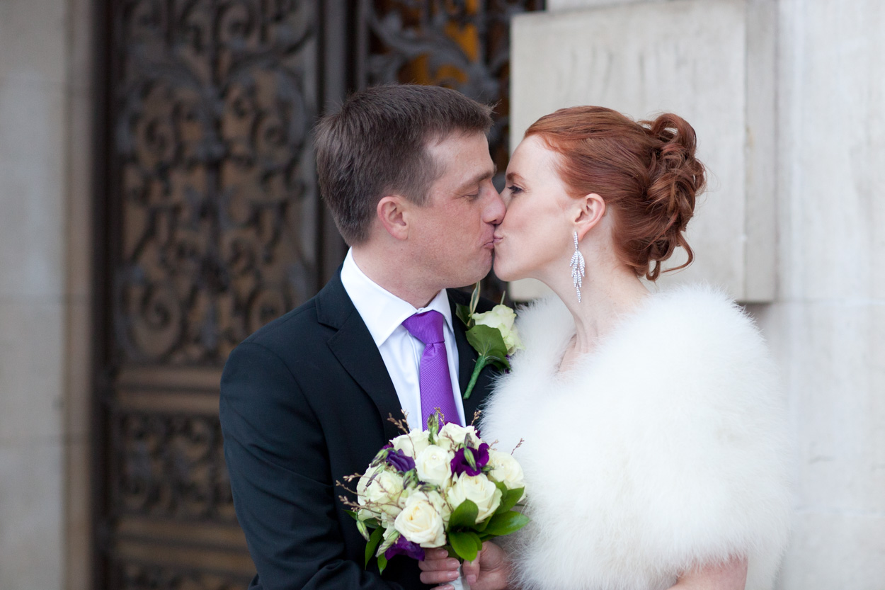 Bride and groom kissing outside the black gates of Leeds Civic Hall in colour.