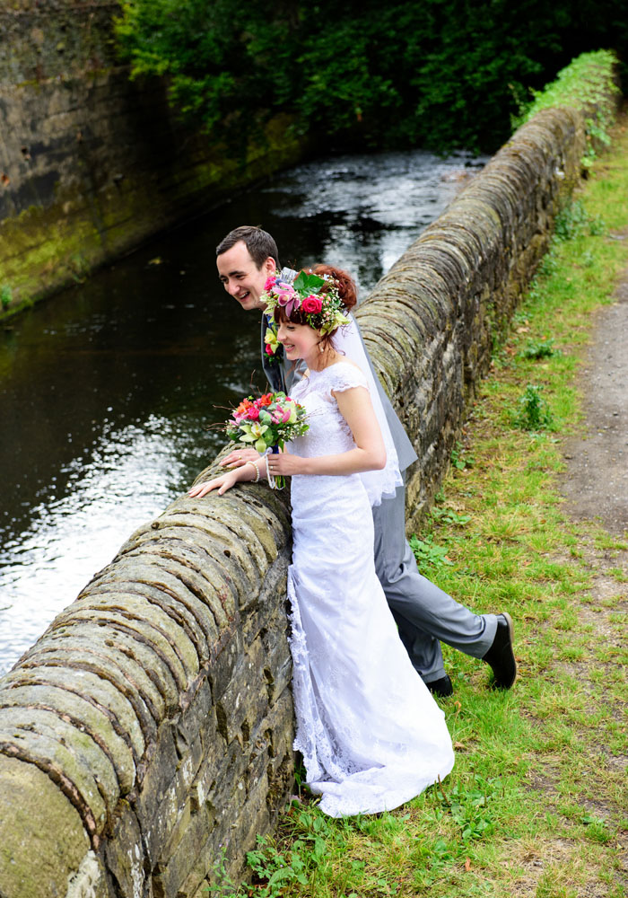 Bride and groom look over a stone wall at the stream beside the church.