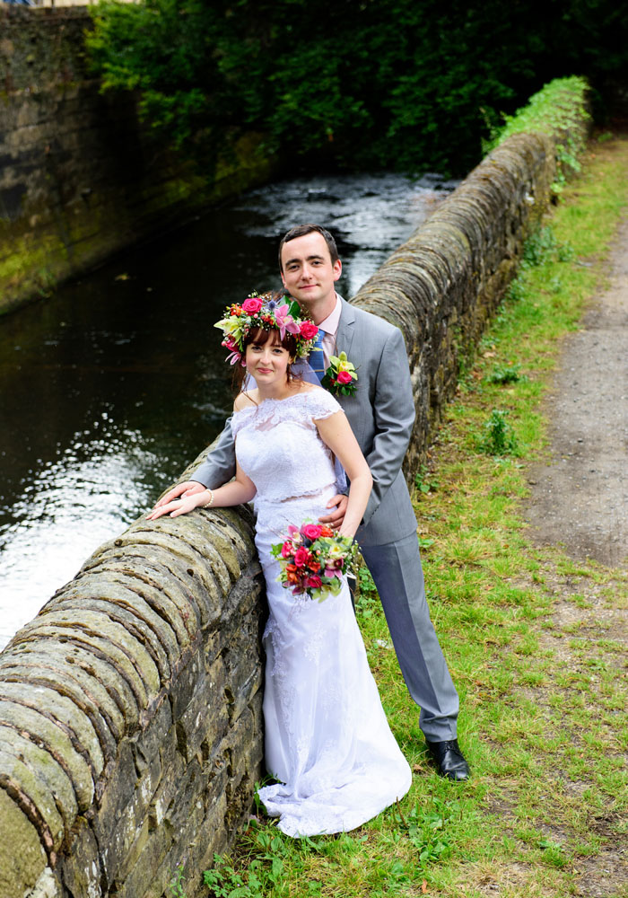 Couple look up at the camera smiling, stream flowing softly behind them.