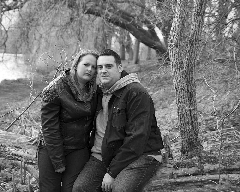 Lisa and Oliver sitting on a fallen tree, sharing subtle smiles in black and white.
