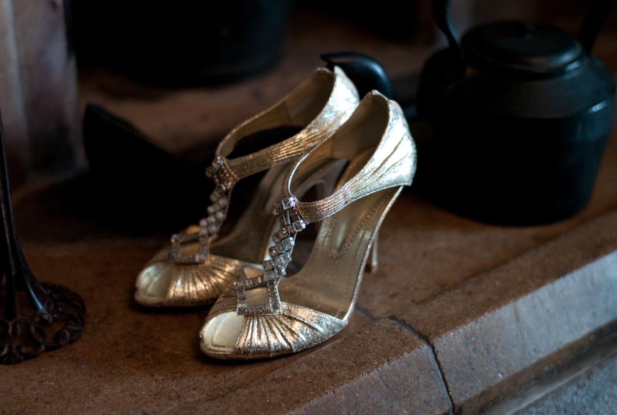 Nikki’s gold wedding heels on the fireplace, contrasting with the dark kettle beside them.