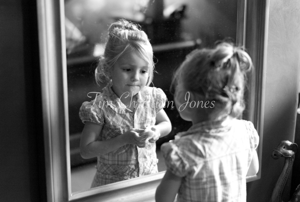 Young girl checks her makeup with focus and flair in black and white.