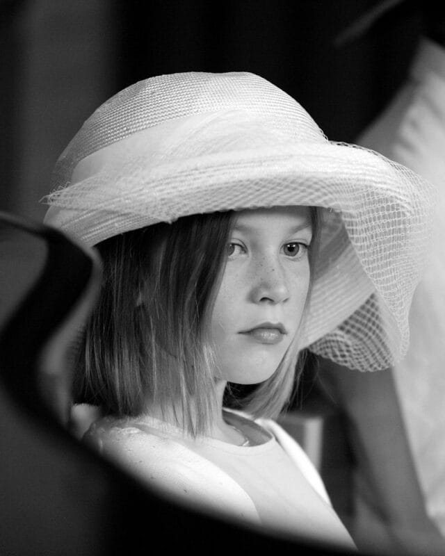 Young girl wearing a hat, sitting thoughtfully in the church pews, lost in her own world
