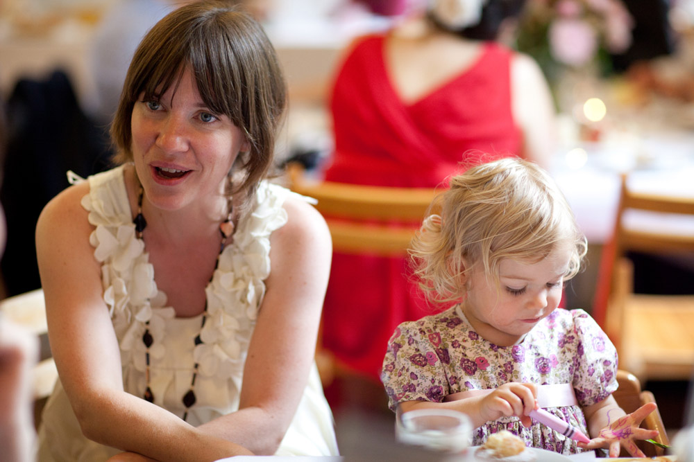 Flower girl colours her fingers with crayons while her mum watches, smiling