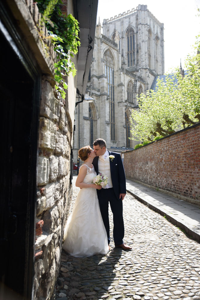 The couple share a kiss on the cobbled road with the minster visible.