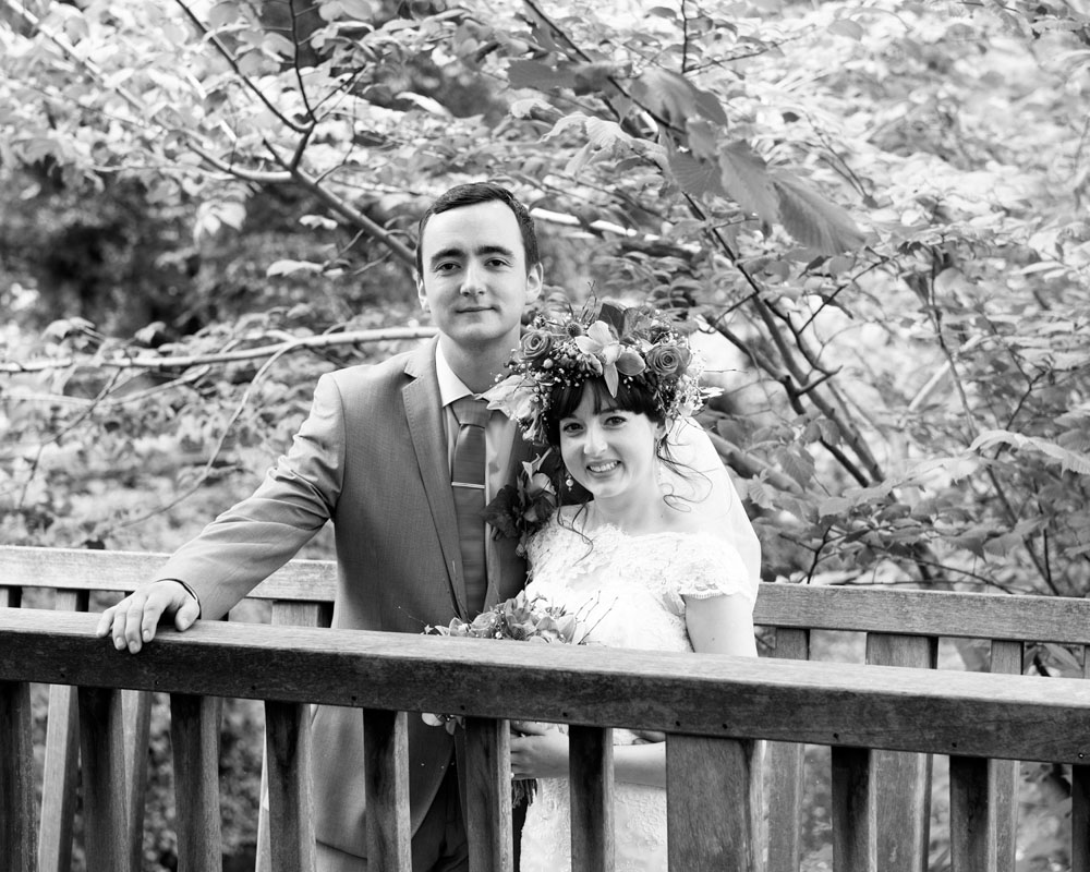 In black and white, the couple smile from the bridge over the water.
