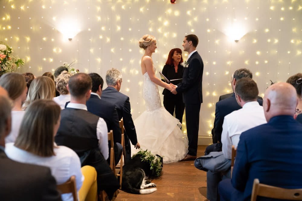 View from the back in colour of the Chilli Barn wedding ceremony, guests and fairy lights framing the moment.