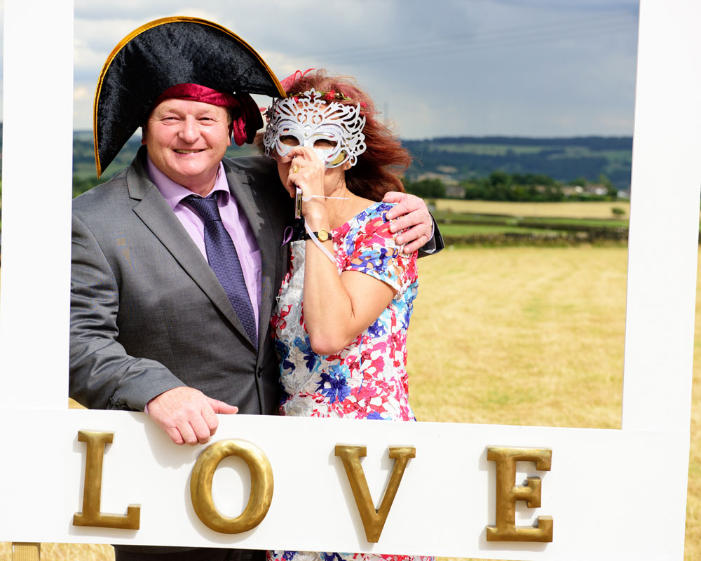 A couple dressed in party hat and deco mask smile in the photo frame at the West Yorkshire reception.