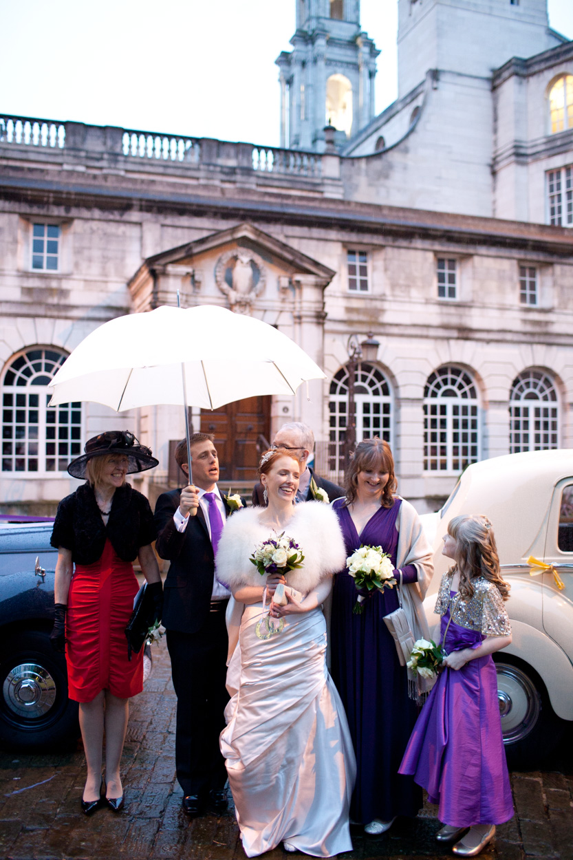 Groom holding a white umbrella over the bride beside the wedding car.