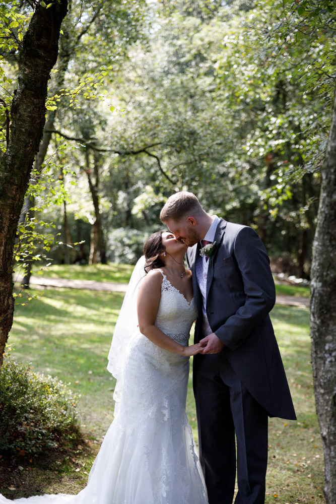 Kyra and Matt kiss in the woodland area of Chevin Lodge, lit beautifully by filtered sunlight.