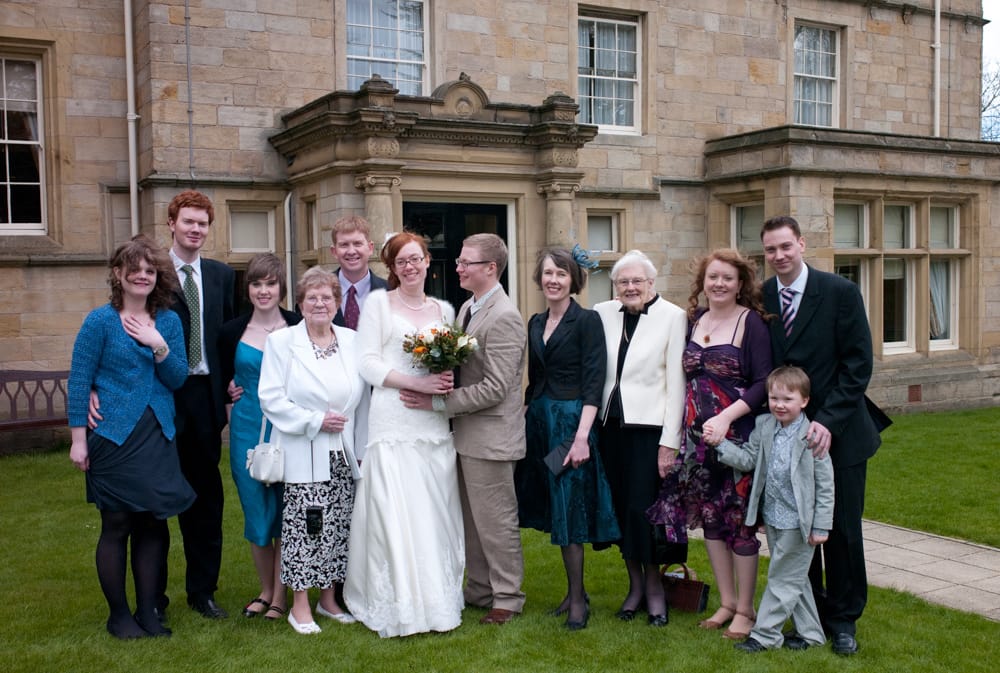 Large family group photo outside Weetwood Hall, wind gently blowing clothes and hair.