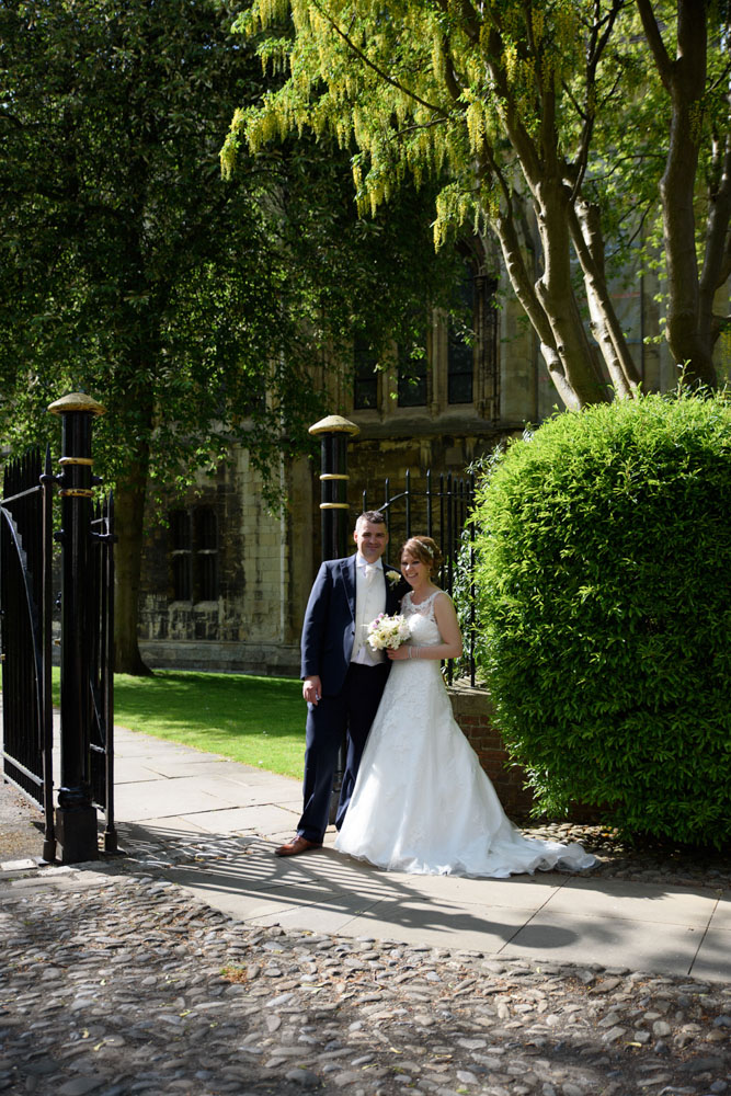 Couple posed by the garden gates with cobbled paths and greenery surrounding them.