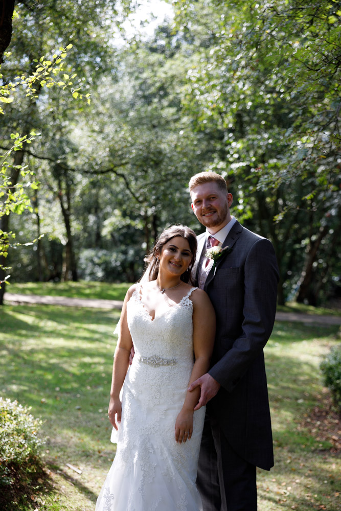 A relaxed portrait of Kyra and Matt smiling in the same woodland spot at Chevin Country Park Hotel.