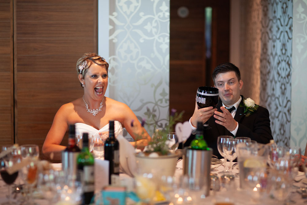 Sam cheers while seated, Tim beside her looking slightly tired but happy.
