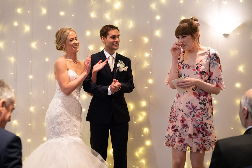 Bride and groom clapping in appreciation as the first reading ends at their Chilli Barn wedding in Otley.