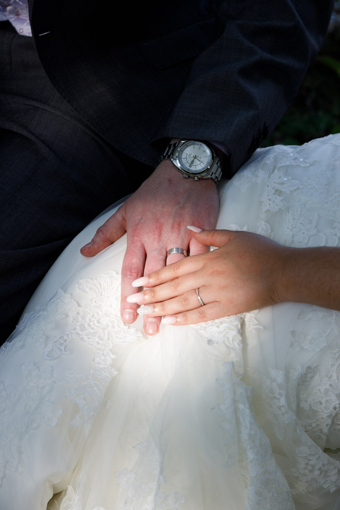 Close-up of the couple’s wedding rings resting in warm sunlight and soft shadow.