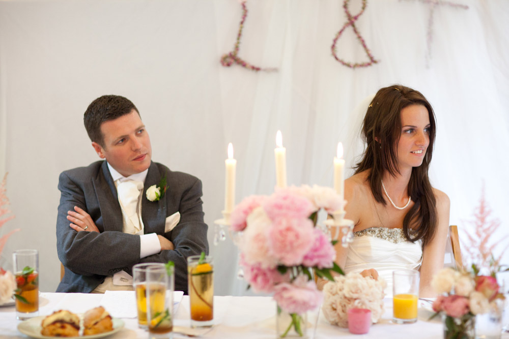 Groom folds his arms and smiles as the bride looks cautiously amused