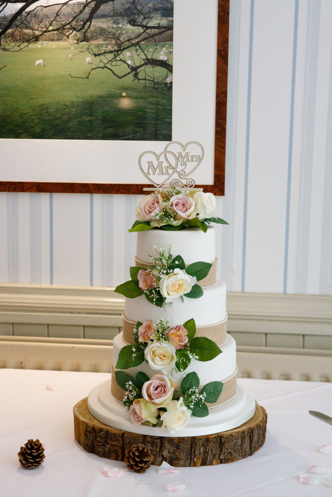 Wedding cake topped with ‘Mr & Mrs,’ decorated with florals, ribbons, and three rustic tiers.