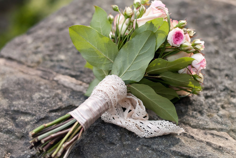Wedding bouquet wrapped in ribbon and lace resting on a stone wall