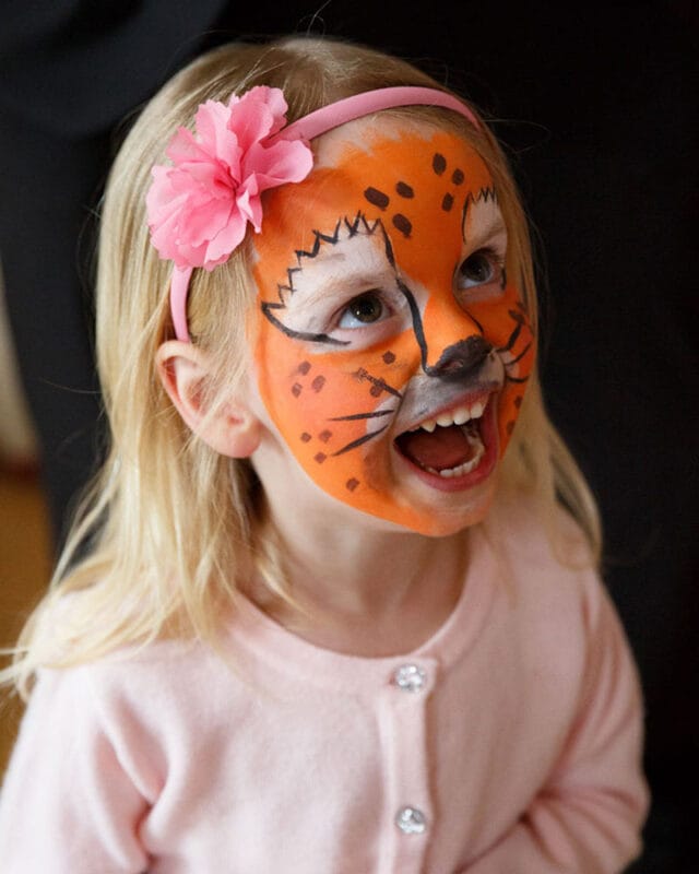 Young girl with lion face paint roaring at her mum at a wedding with lots of children