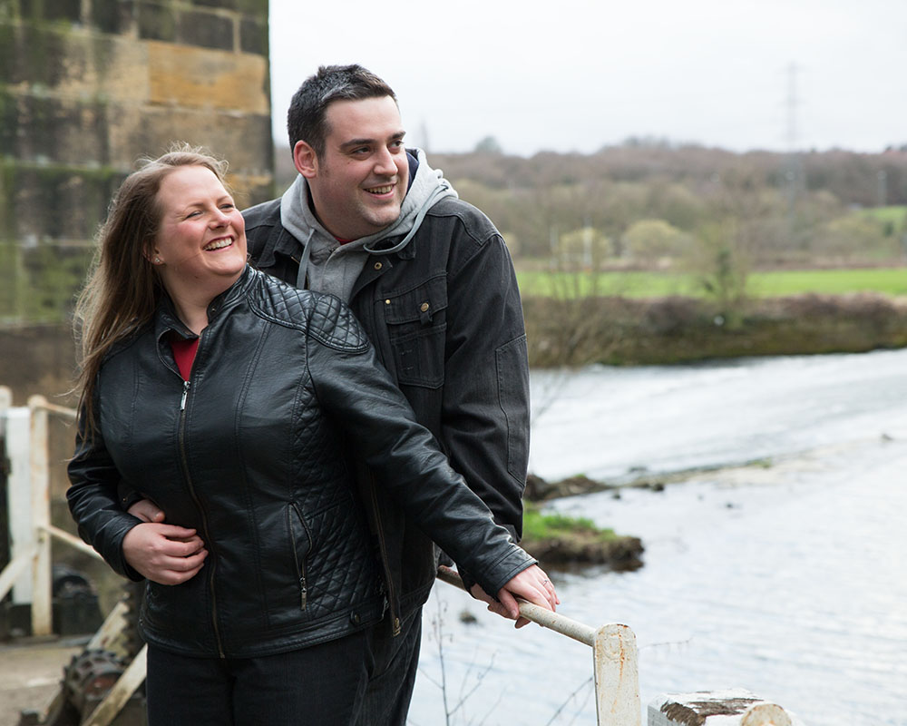 Lisa and Oliver standing close together, looking over the weir at Kirkstall.