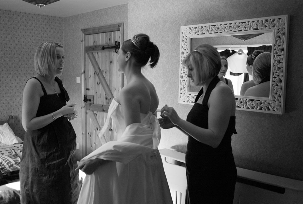 Alison smiles as one sister ties the back of her wedding dress.
