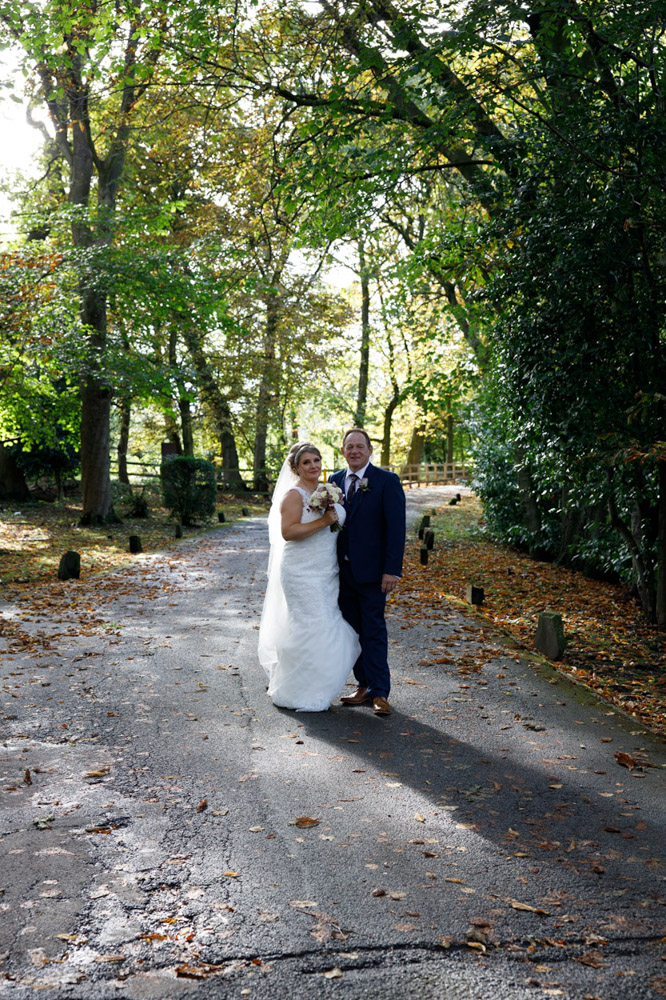 Couple stood beneath an arch of trees on the entrance road