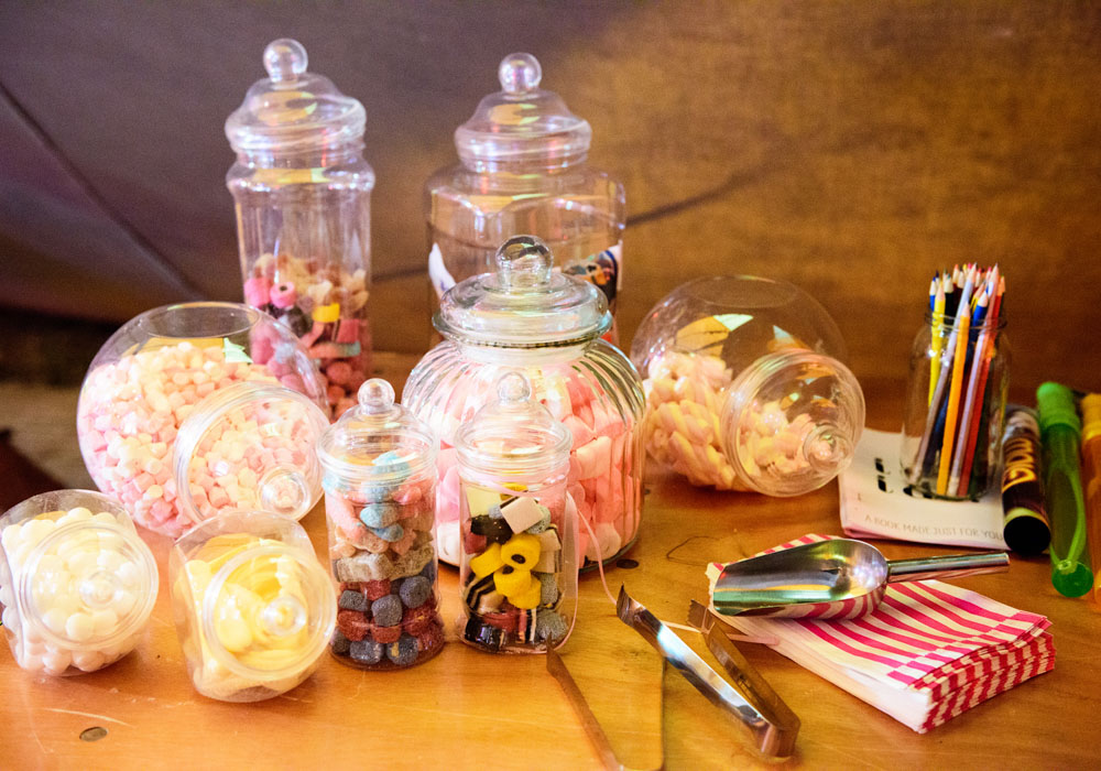 Sweet table filled with treats, kisses sign, and pastel decor inside the tent.