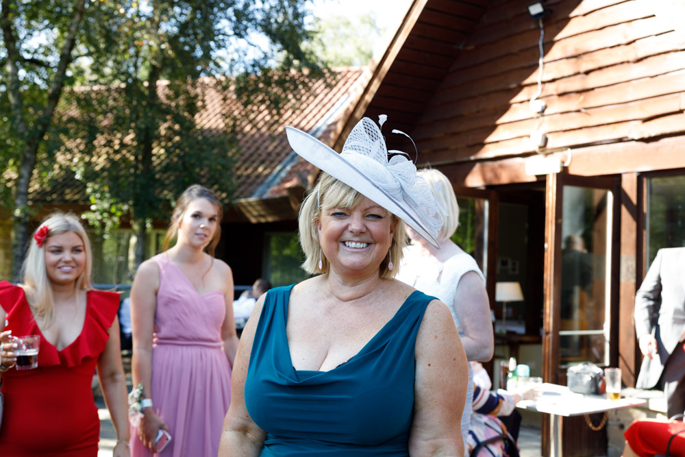 A wedding guest in a pink hat notices the camera and smiles warmly for a candid photo.